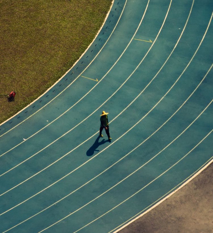 Laufbahn eines Stadions von oben, ein einzelner Läufer auf der Geraden.